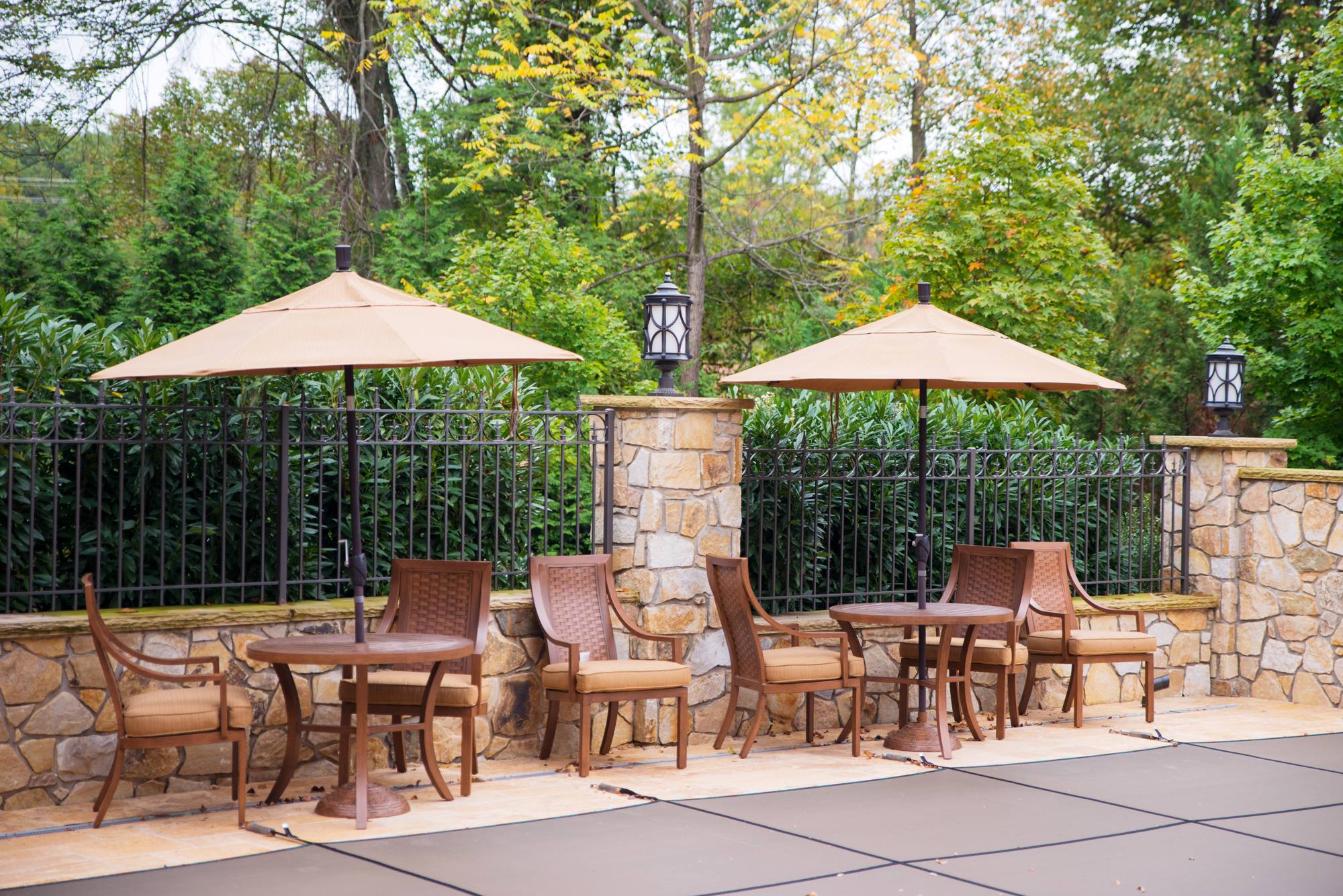 Travertine poolside patio with umbrella dining by stone pillars in Northern Virginia
