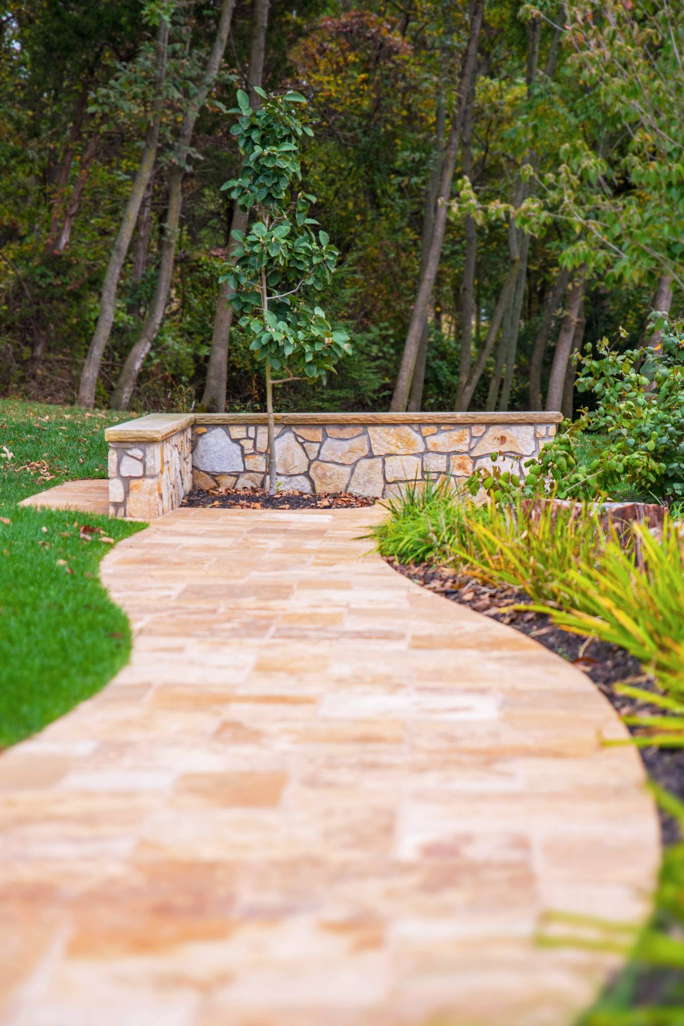 Travertine walkway curving past a stone garden wall in Northern Virginia